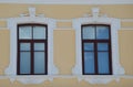 Two windows on the yellow facade of a restored building. Closed windows in a brown frame, with white trim. Element of