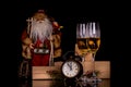 Two wine glasses with champagne, Santa Claus, clock and christmas gifts on a black background Royalty Free Stock Photo