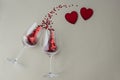 Two wine glasses with little red heart sparkling confetti and two transparent heart on top of image on light background, lots of c Royalty Free Stock Photo