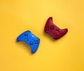 Two wireless gamepads red and blue lie on a yellow background. Confrontation of players,