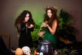 Two witches with rats in their hands pose against a dark background