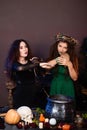 Two witches with rats in their hands pose against a dark background