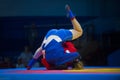 Two woman in blue and red wrestling on a yellow wrestling carpet in the gym