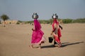 Two woman carrying water in steel vessels on head in desert, Khuri,