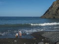 Two woman and child from back at Playa de Vallehermoso, volcanic black sand beach with pebbles and mountain cliff with