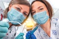 Two woman dentists in medical masks standing right above the patient, holding tools and ready to start working, dentistry and