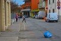 Two woman on an empty street with white cars parked on the side. Blue garbage bag in the middle of the road