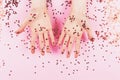 Two woman hands and falling confetti on pink background.