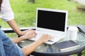 Two woman are seeing laptop on glass table while typing on pad with black note and coffee paper cup in green grass background. Royalty Free Stock Photo