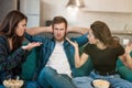 Two women arguing with their friend man sitting together on the sofa, opposite sexes concept