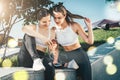 Two women athletes in sportswear sitting in park, relax after sports training, use smartphone, listening to music. Royalty Free Stock Photo