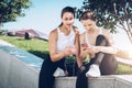 Two women athletes in sportswear sitting in park, relax after sports training, use smartphone, listening to music. Royalty Free Stock Photo