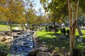 Two women with baby stroller sitting on lush green grass in the park surrounded by autumn trees near a running river Royalty Free Stock Photo