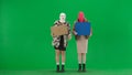 Two women in balaclavas and faux fur coats picketing in the studio on the green screen. Women point to posters and