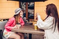 Two women chatting while having coffe in outdoor cafe. Happy friends using phone checking pictures. Girls hang out