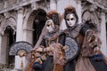 Masked women in costume, with decorated fans, standing in front of the arches at St Marks Square during the Venice Carnival