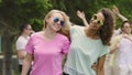 Two women dancing, hugging, enjoying concert with friends in park, youthfulness