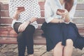 Two women in disinterest moment with smart phones in the outdoor, concept of relationship apathy and using new technology.