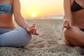 Two women doing group meditation on the beach on sunrise. Female friends doing yoga padmasana or lotus asana sitting on Royalty Free Stock Photo