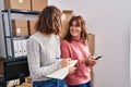 Two women ecommerce business workers writing on notebook using smartphone at office Royalty Free Stock Photo