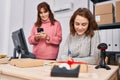 Two women ecommerce business workers writing on notebook using smartphone at office Royalty Free Stock Photo