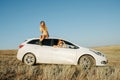 Two women enjoying views of steppe. one sitting on a car roof, other is a driver