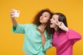 Two women friends european african girls in pink green clothes posing isolated on yellow background. People lifestyle Royalty Free Stock Photo