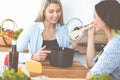 Two women friends looking into the dark pot with a ready meal and taste new recipes while sitting at the kitchen table Royalty Free Stock Photo