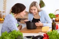 Two women friends looking into the dark pot with a ready meal and taste new recipes while sitting at the kitchen table Royalty Free Stock Photo