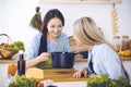 Two women friends looking into the dark pot with a ready meal and taste new recipes while sitting at the kitchen table Royalty Free Stock Photo