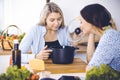 Two women friends looking into the dark pot with a ready meal and taste new recipes while sitting at the kitchen table Royalty Free Stock Photo