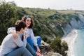 Two women friends sitting, laughing and looking at beautiful sea landscape on top of the mountain. Friendship and nature concept Royalty Free Stock Photo