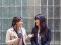 Two women friends sitting outside laughing while drinking a take-away coffee. Royalty Free Stock Photo