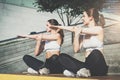 Two women, girls in sportswear doing stretching exercises while listening to music. Workout, couching on city street. Royalty Free Stock Photo