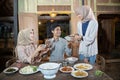 two women in headscarves and an asian man tidying the dining table after iftar together