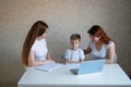 Two women help the boy do school homework. Female tutor teaches a child at home in the kitchen. The school teacher