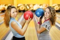 Two women hold balls and smile in bowling club