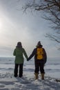 Two woman holding hands with backs turned on frozen lake shore p