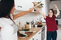 Two woman image that they are fighting on swords by wooden spatulas in kitchen