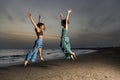 Two women jump one in front of the other at sunset on the beach expressing their joy of living. Royalty Free Stock Photo