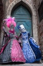 Two women in masks and ornate blue and pink costumes standing in front of an old blue door in Venice during the Carnival Royalty Free Stock Photo