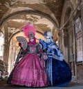 Two women in masks and ornate blue and pink costumes standing under the arches in the Railto Market, Venice during carnival