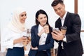 Two women and a man are drinking coffee and watching something on the phone screen. Royalty Free Stock Photo