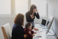 two women in office outfit working on computers and discussing a report on the floor; one of them is with a baby girl in her arms Royalty Free Stock Photo