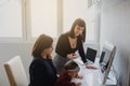 two women in office outfit working on computers and discussing a report on the floor; one of them is with a baby girl in her arms Royalty Free Stock Photo