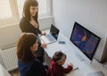 two women in office outfit working on computers and discussing a report on the floor; one of them is with a baby girl in her arms Royalty Free Stock Photo