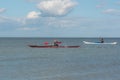 Two women paddling a red and a white kayak in wide ocean