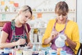 Two women painting own ceramic tableware in DIY workshop