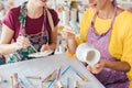 Two women painting own ceramic tableware in DIY workshop