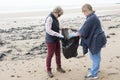 Two women picking up rubbish from a beach